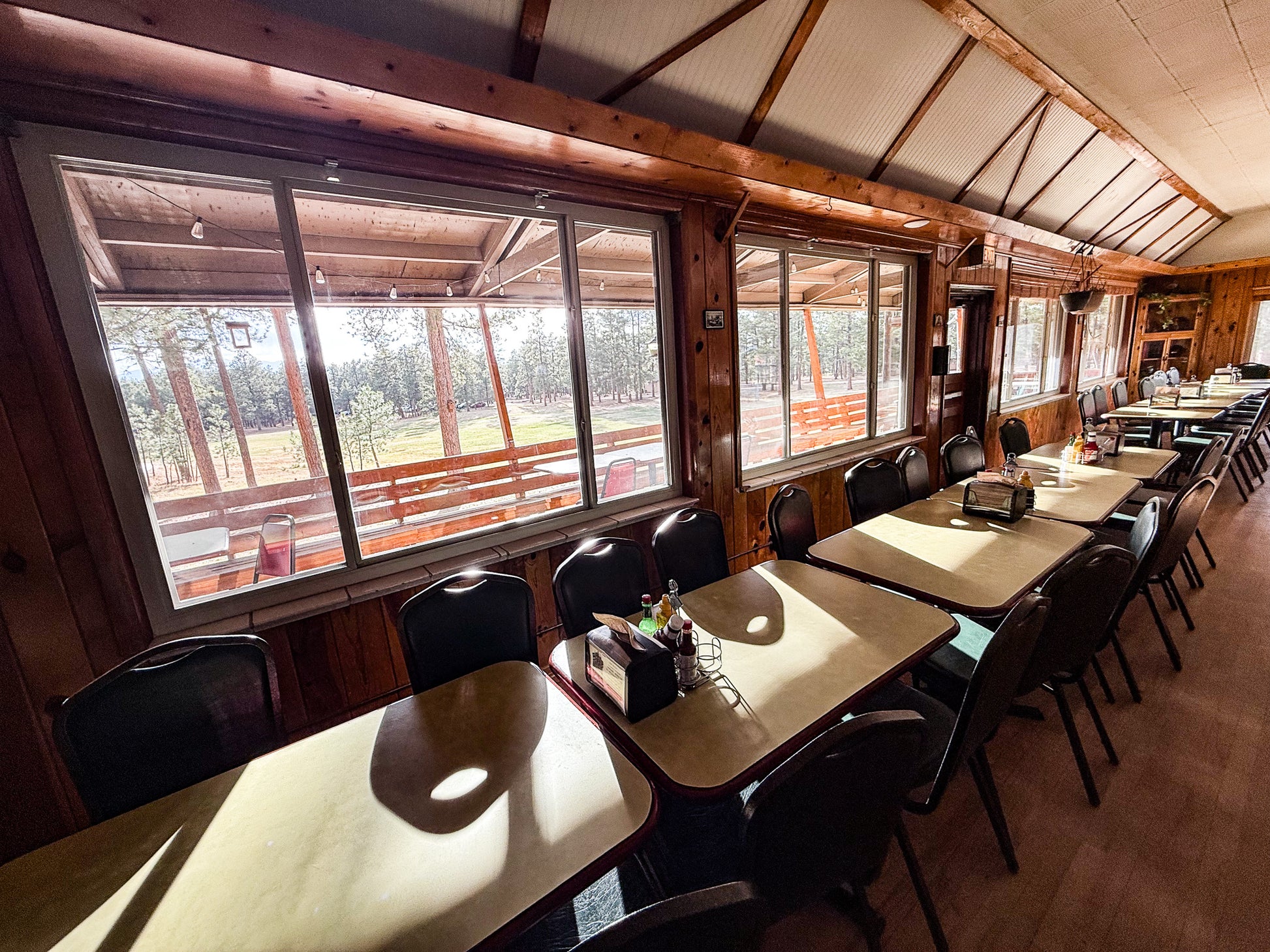 Dining hall with wooden tables and chairs in a rustic setting with large windows. Creepaway Camp, La Foret Conference and Retreat Center, Black Forest, Colorado.